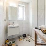 Petite salle de bain en rénovation, outils rangés proprement, meuble vasque simple et ambiance de chantier lumineuse.