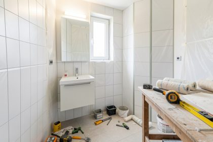 Petite salle de bain en rénovation, outils rangés proprement, meuble vasque simple et ambiance de chantier lumineuse.