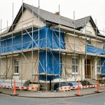 Maison en rénovation extérieure avec échafaudage sécurisé, bâches de protection et zone de chantier soigneusement délimitée.