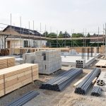 Chantier de construction résidentielle de gros œuvre, propre et organisé, avec matériaux rangés, coffrages, échafaudages et engins éclairés par la lumière naturelle.